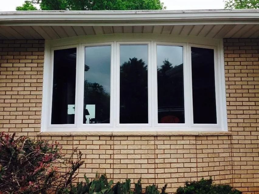 Bay window with white trim on a brick house. Trees are reflected in the glass.