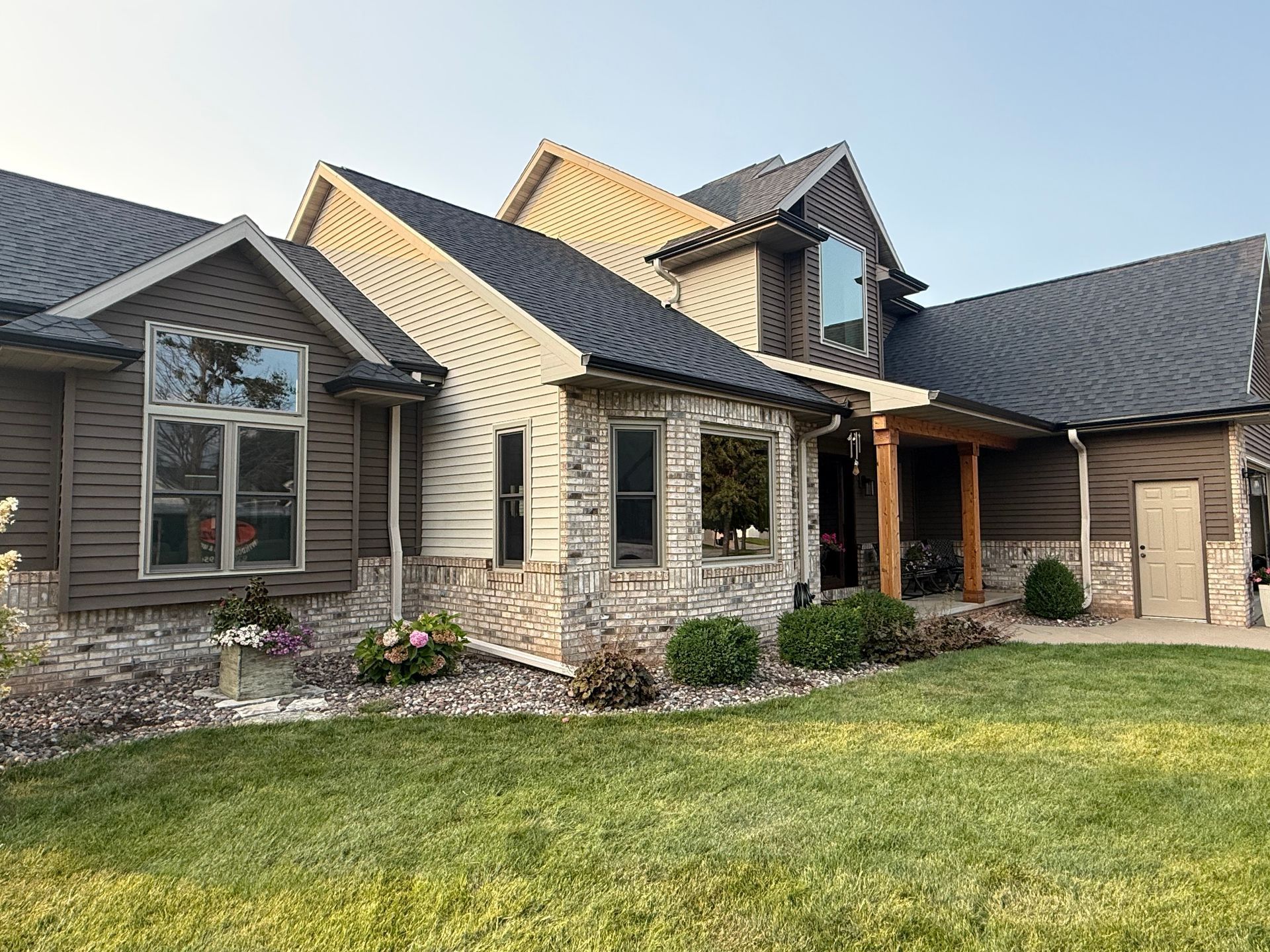 Suburban house exterior with stone and dark siding, gabled roof, front porch, and green lawn.