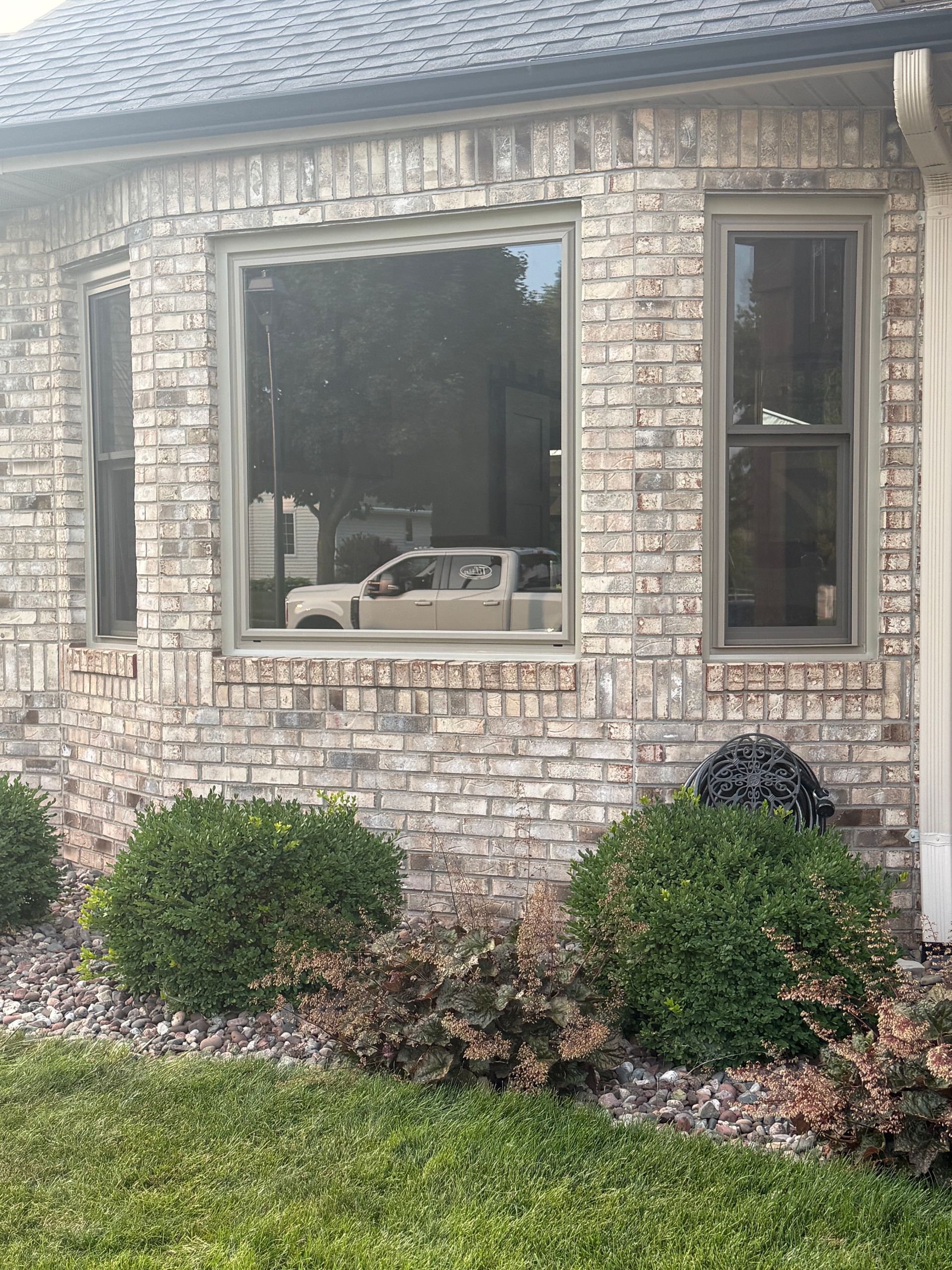 Brick house exterior with large window, small shrubs, and lawn in front