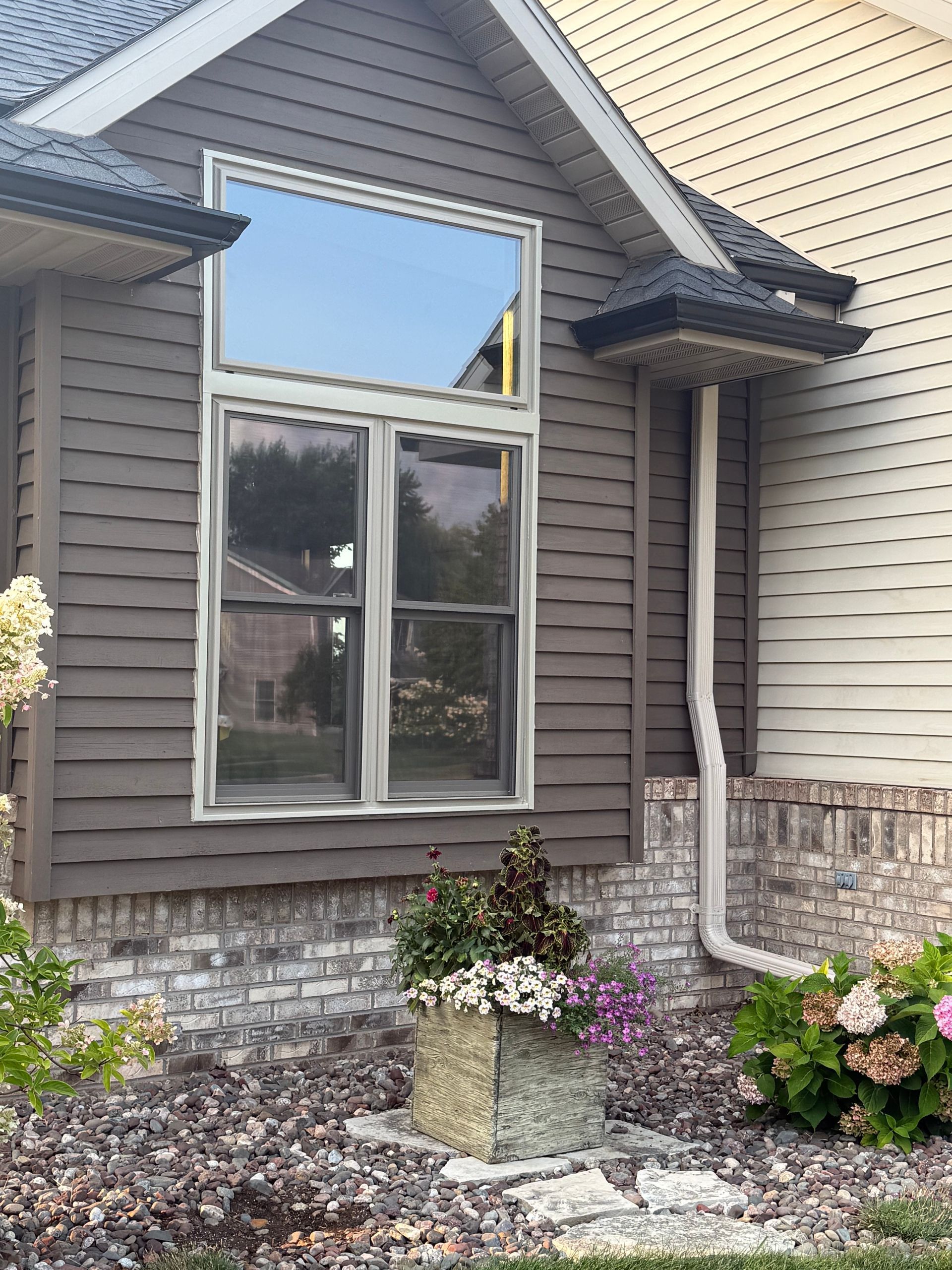 Exterior of a house with a bay window, beige siding, stone foundation, and flower beds below