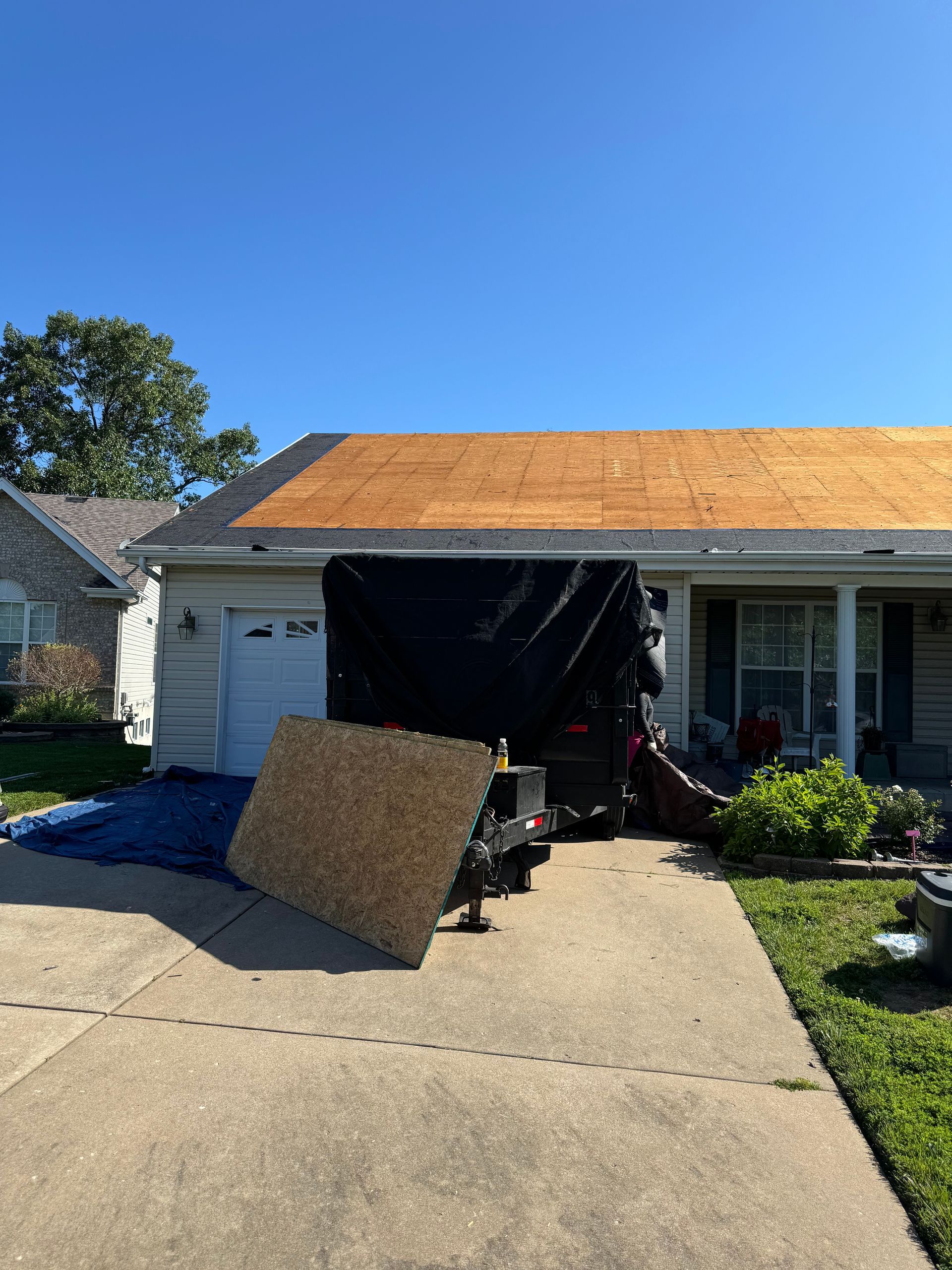 A house with a roof that is being repaired and a trailer parked in front of it.