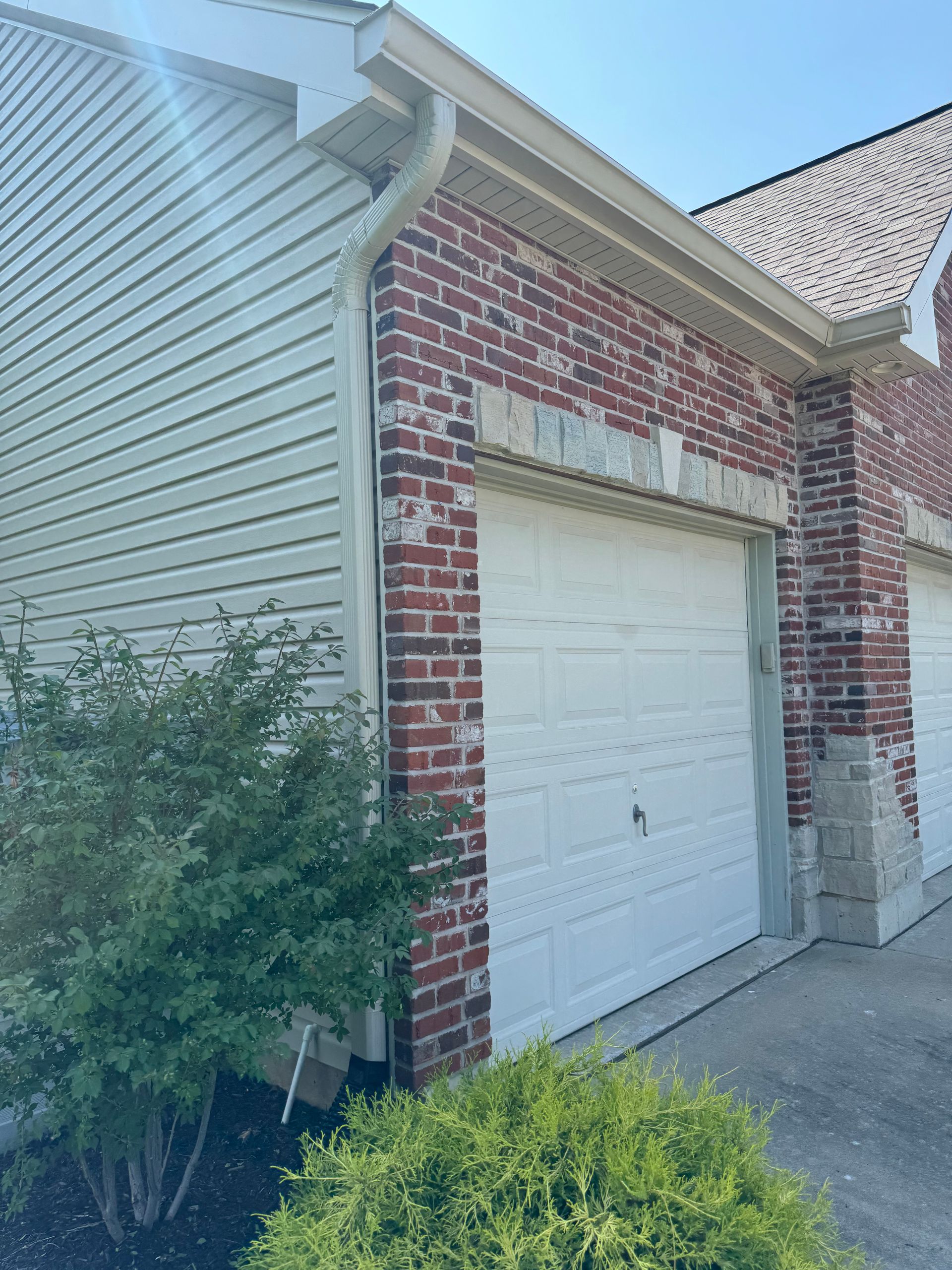 A brick house with two white garage doors and a white siding.