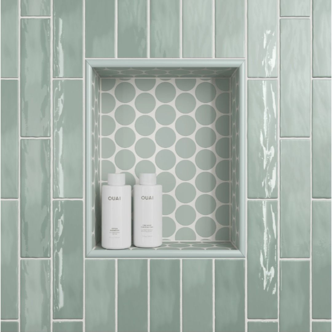 Shower niche with white and green tiles. Two white bottles sit on a shelf.
