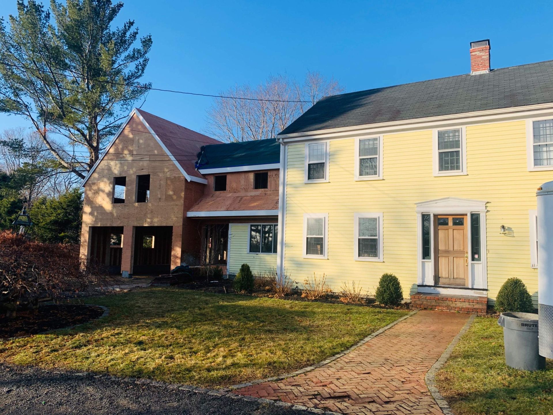 A yellow house with a new addition under construction; a brick pathway leads to the front door.