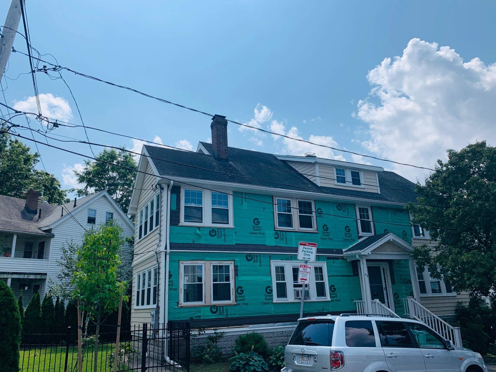 Three-story house under construction with blue wrap, white trim, and a car parked in front.