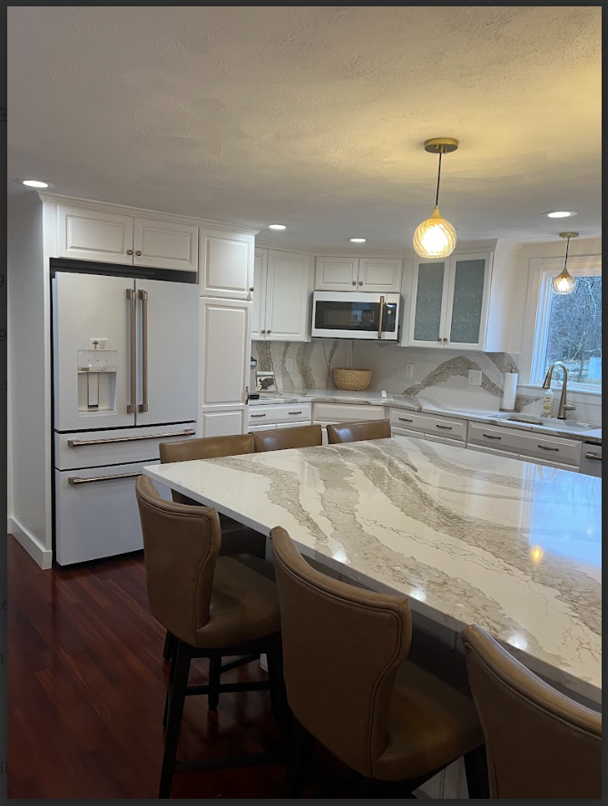 Modern white kitchen with island, marble countertops, stainless steel appliances, dark wood floors, and leather bar stools.