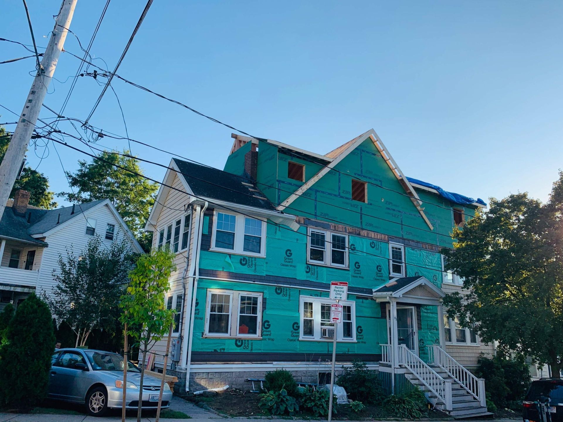 Two-story house under construction, covered in green material, with a blue sky background.
