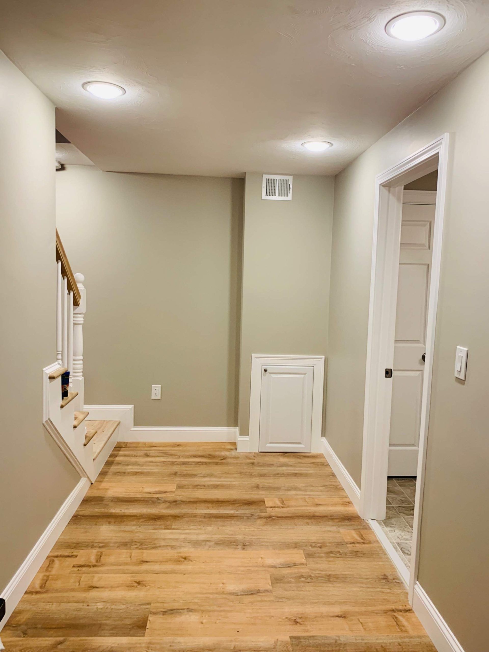 Hallway with wood floors, neutral walls, stairs on left, door on right, recessed lighting.