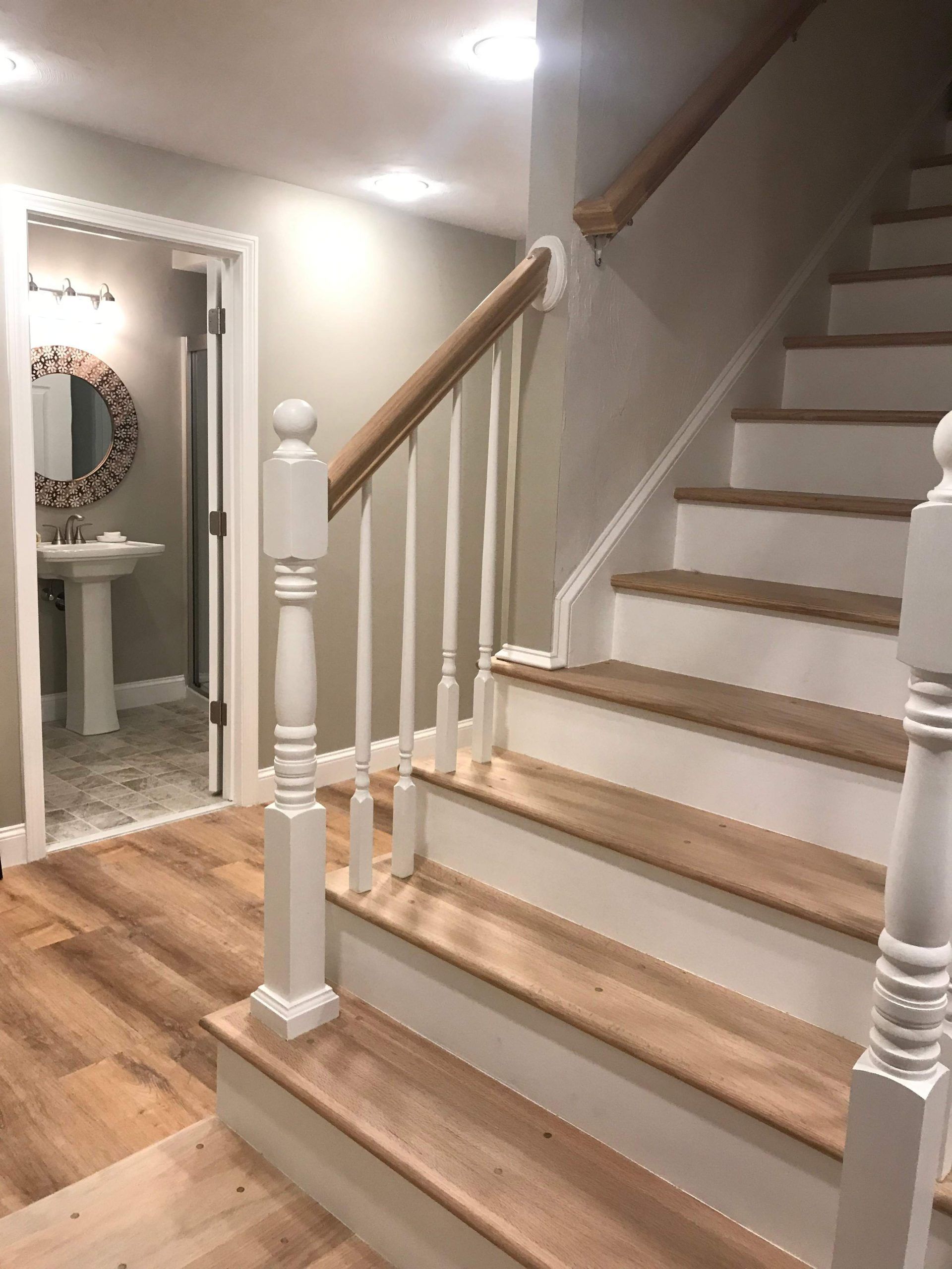 Staircase with light wood steps and white risers, leading to a bathroom with a sink and mirror.