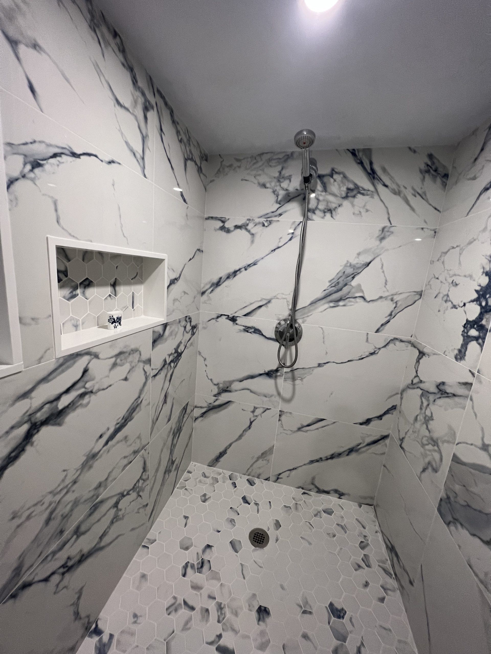 Shower with white marble-patterned walls, a mosaic tile floor, and a built-in shelf.