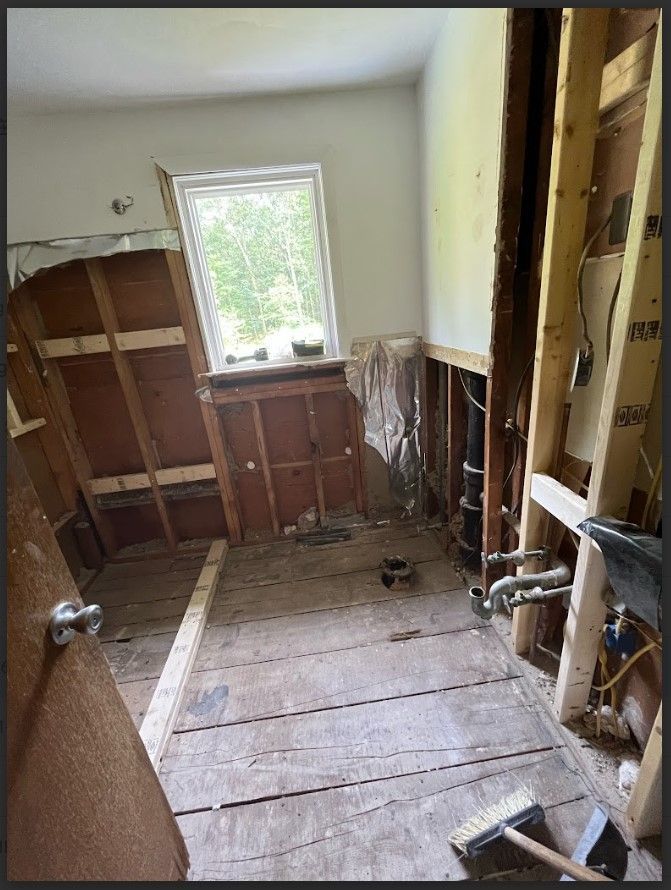 Bathroom under renovation with exposed studs, window, and plumbing.