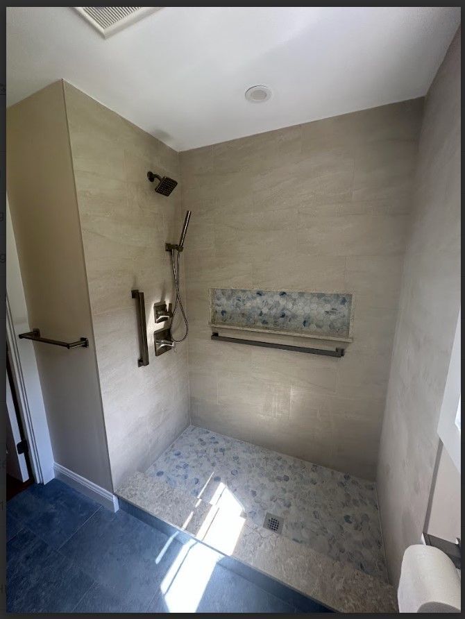 A modern shower with beige walls, pebble floor, and dark fixtures; includes a grab bar.
