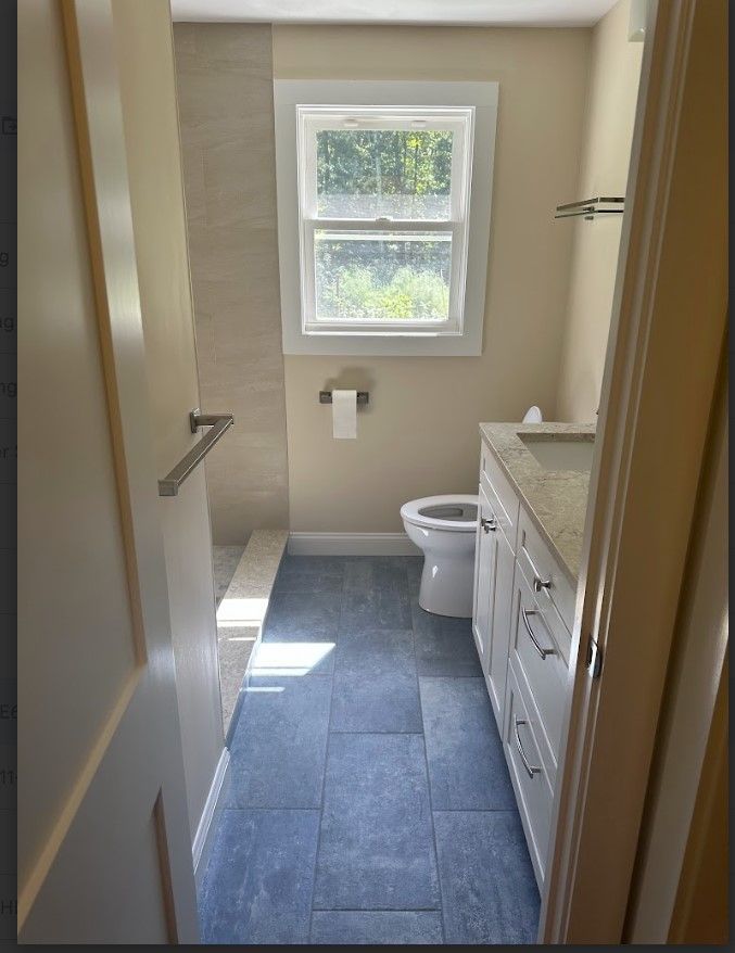 Bathroom with blue tiled floor, white vanity, toilet, and window. Light beige walls.