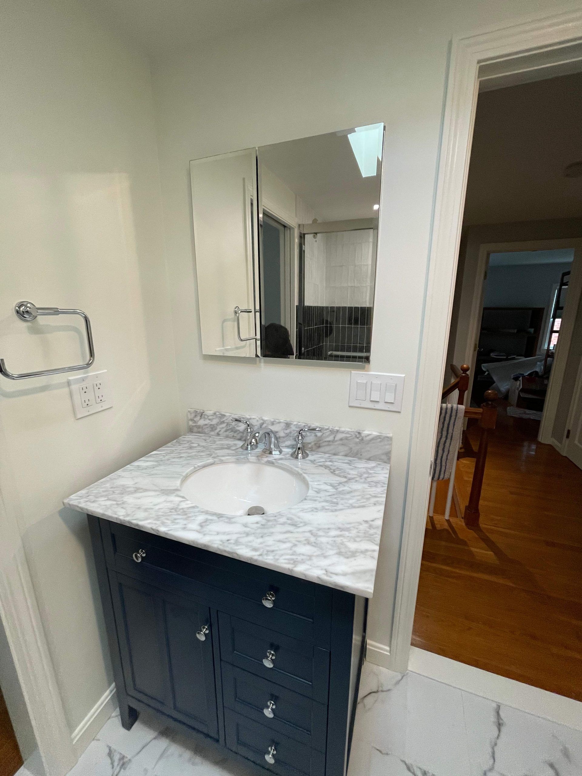 Navy blue vanity with marble countertop and a mirror in a bathroom.
