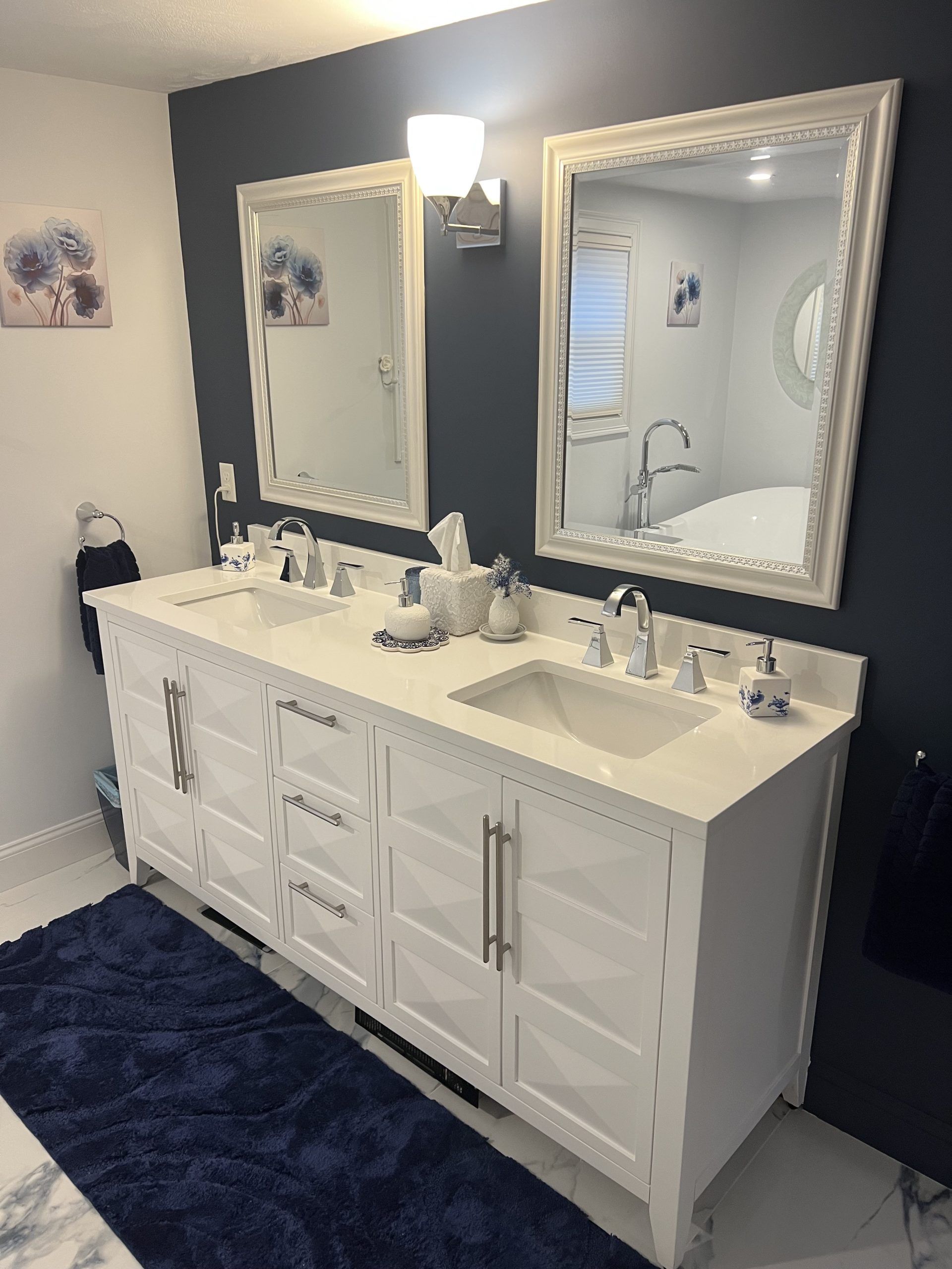 White double vanity with two mirrors, dark blue wall, and blue rug.