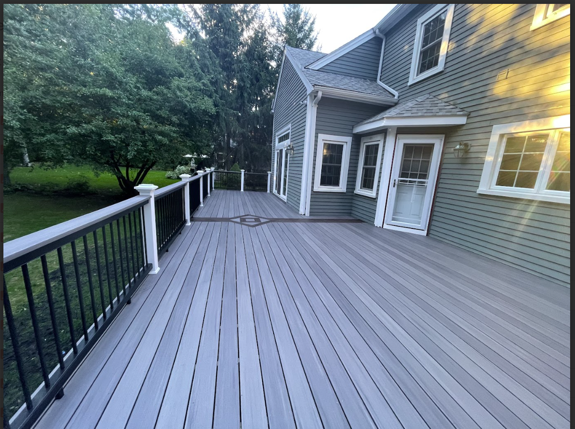 Gray composite deck attached to a two-story house with green siding and black railings.