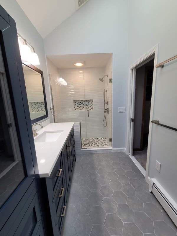 Modern bathroom with blue vanity, white shower, and gray hexagon floor tiles.