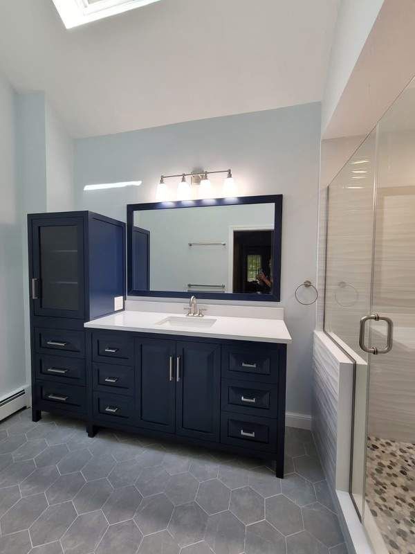Blue bathroom vanity with matching cabinet and hexagon tile floor. Shower with glass door.