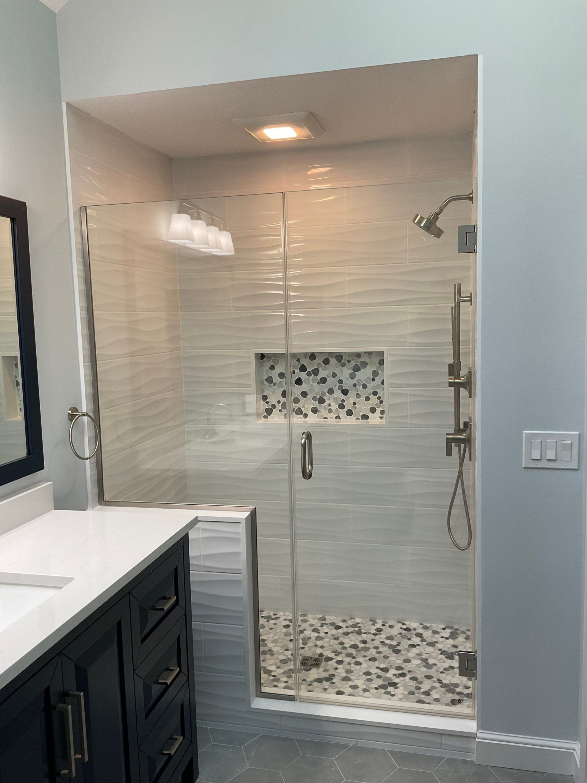 Glass shower enclosure with gray textured tile, recessed niche, and stone floor.
