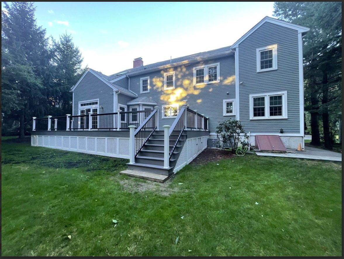 Rear view of a two-story gray house with a large wooden deck and a green lawn in front.