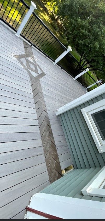Overhead view of a deck with light gray decking and a darker chevron-patterned inset, with a black railing.