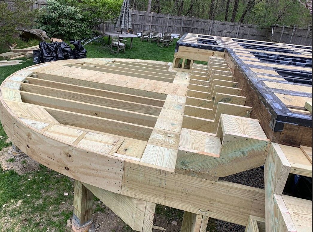 Partially built wooden deck with curved edges and steps in an outdoor setting.