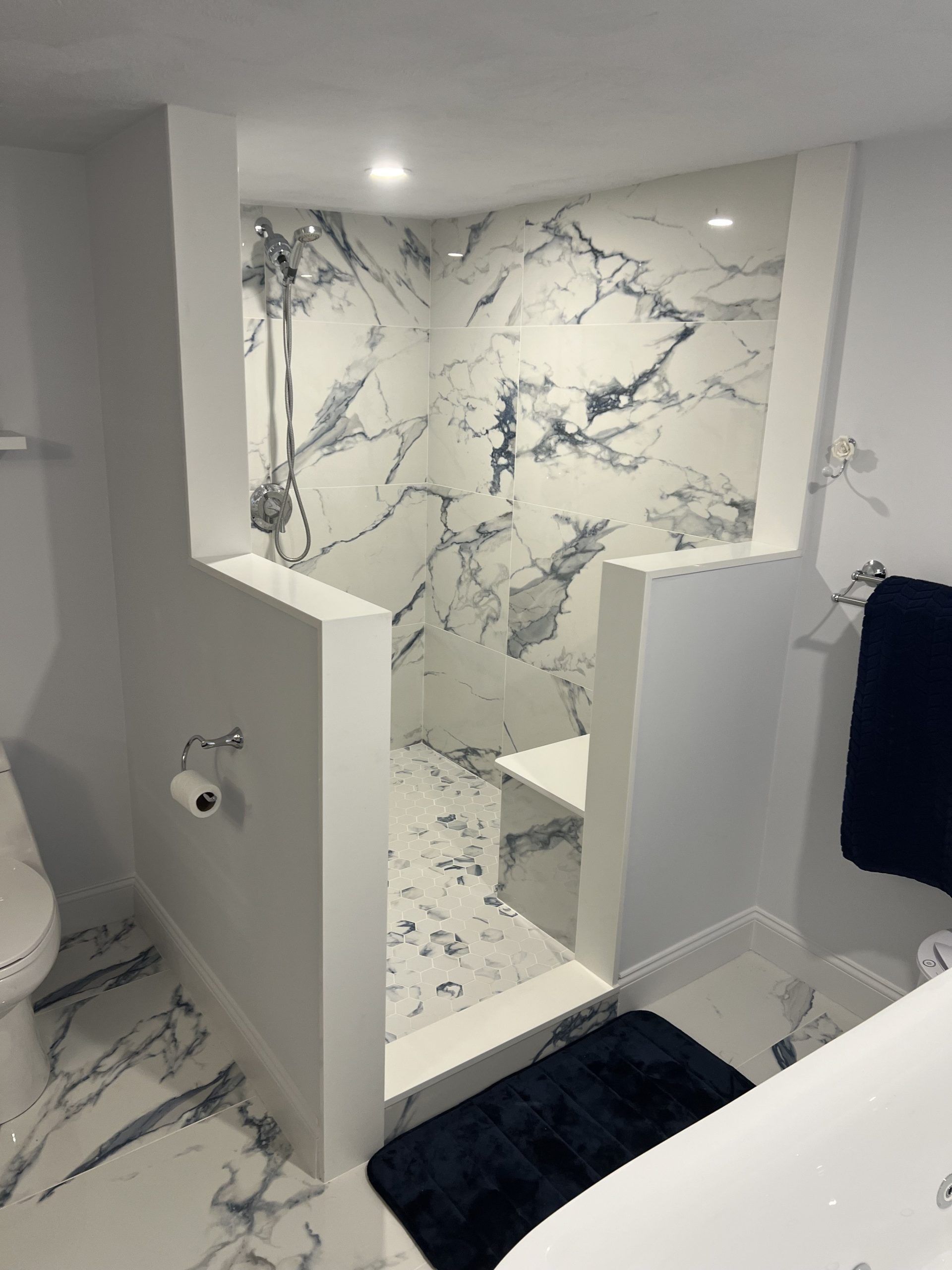 Walk-in shower with marble tile, a built-in seat, and white walls.