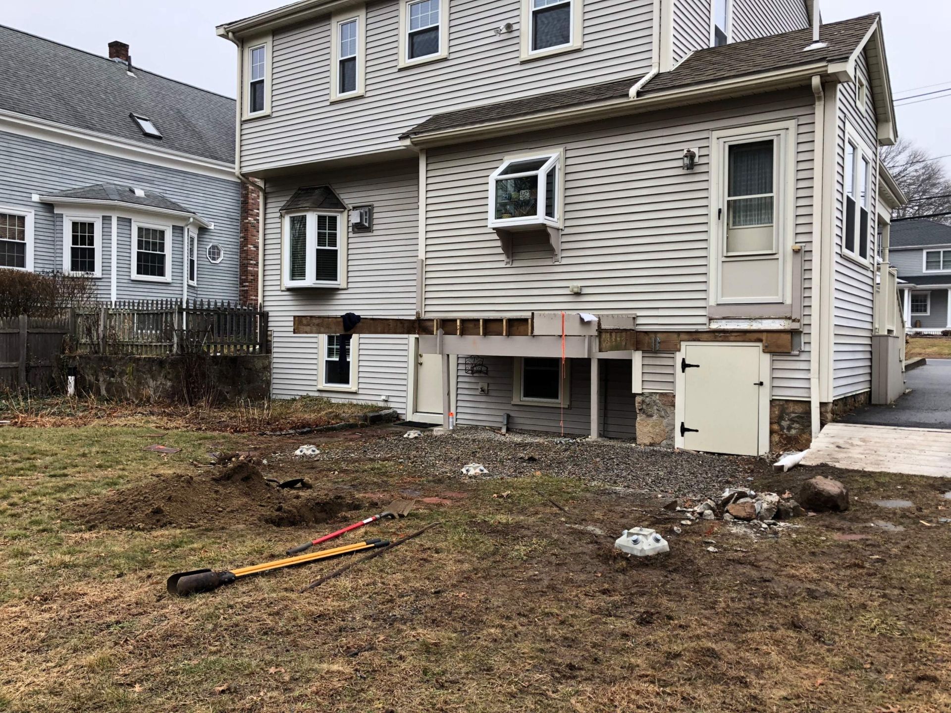 Rear exterior of a house with exposed foundation and a partially built deck; yard with dirt and debris.