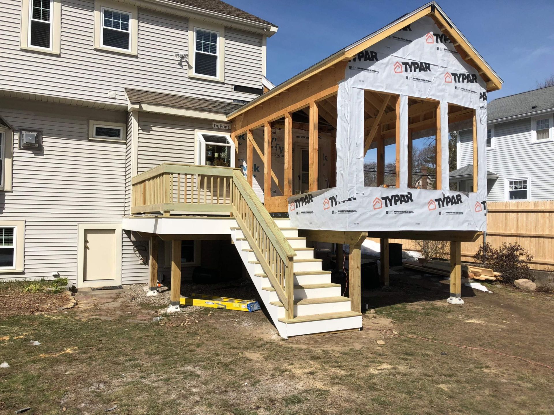 A sunroom being built onto a house, with a deck and stairs.  The structure is under construction, using Typar wrap.