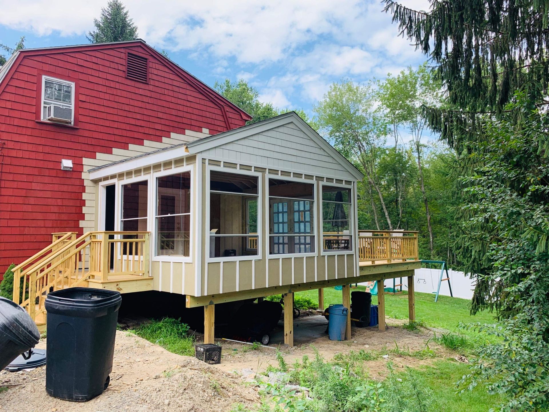 A newly constructed beige screened porch with a wooden deck attached to a red house.