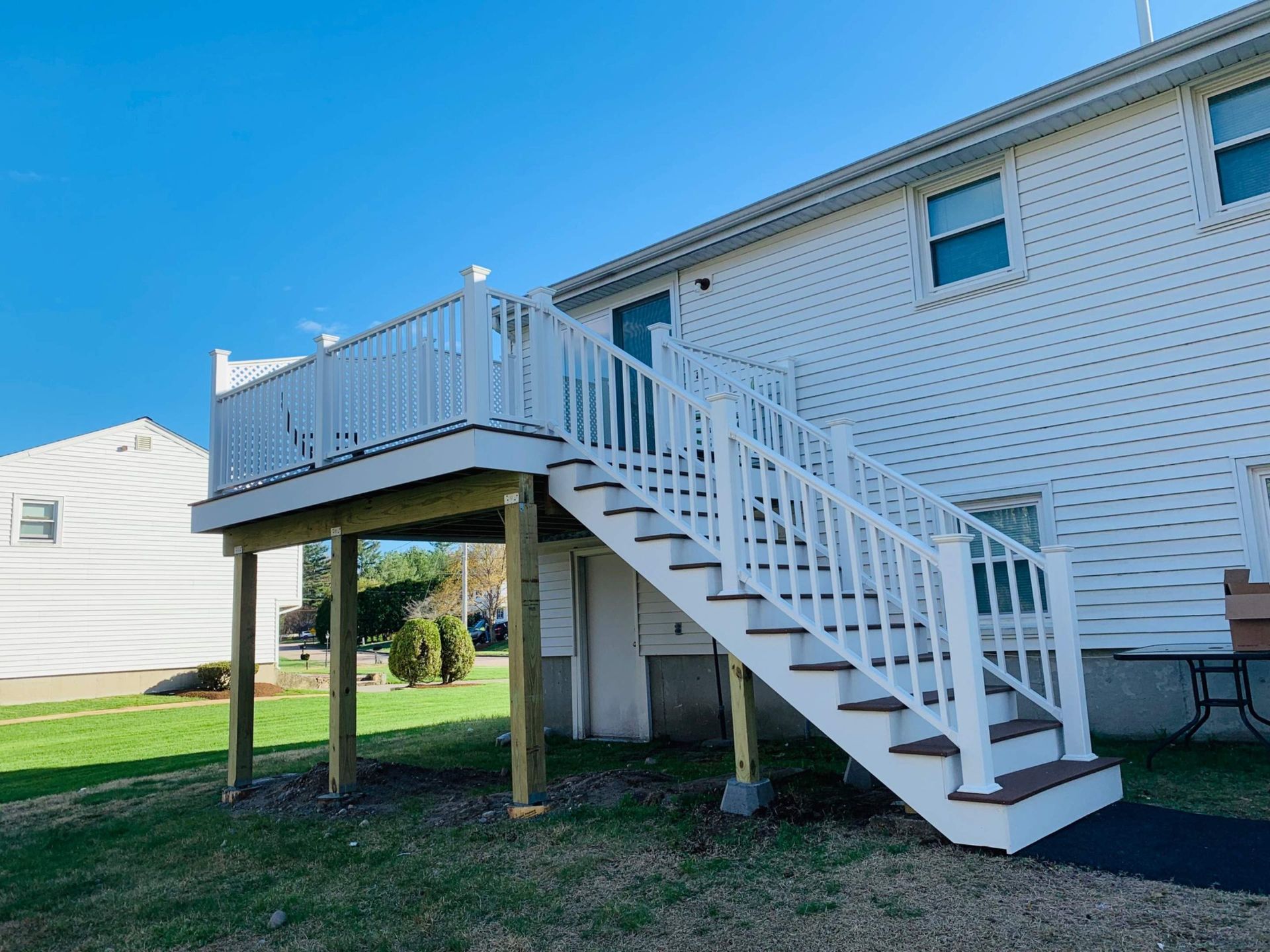 White deck and stairs attached to a two-story building on a grassy lawn under a blue sky.