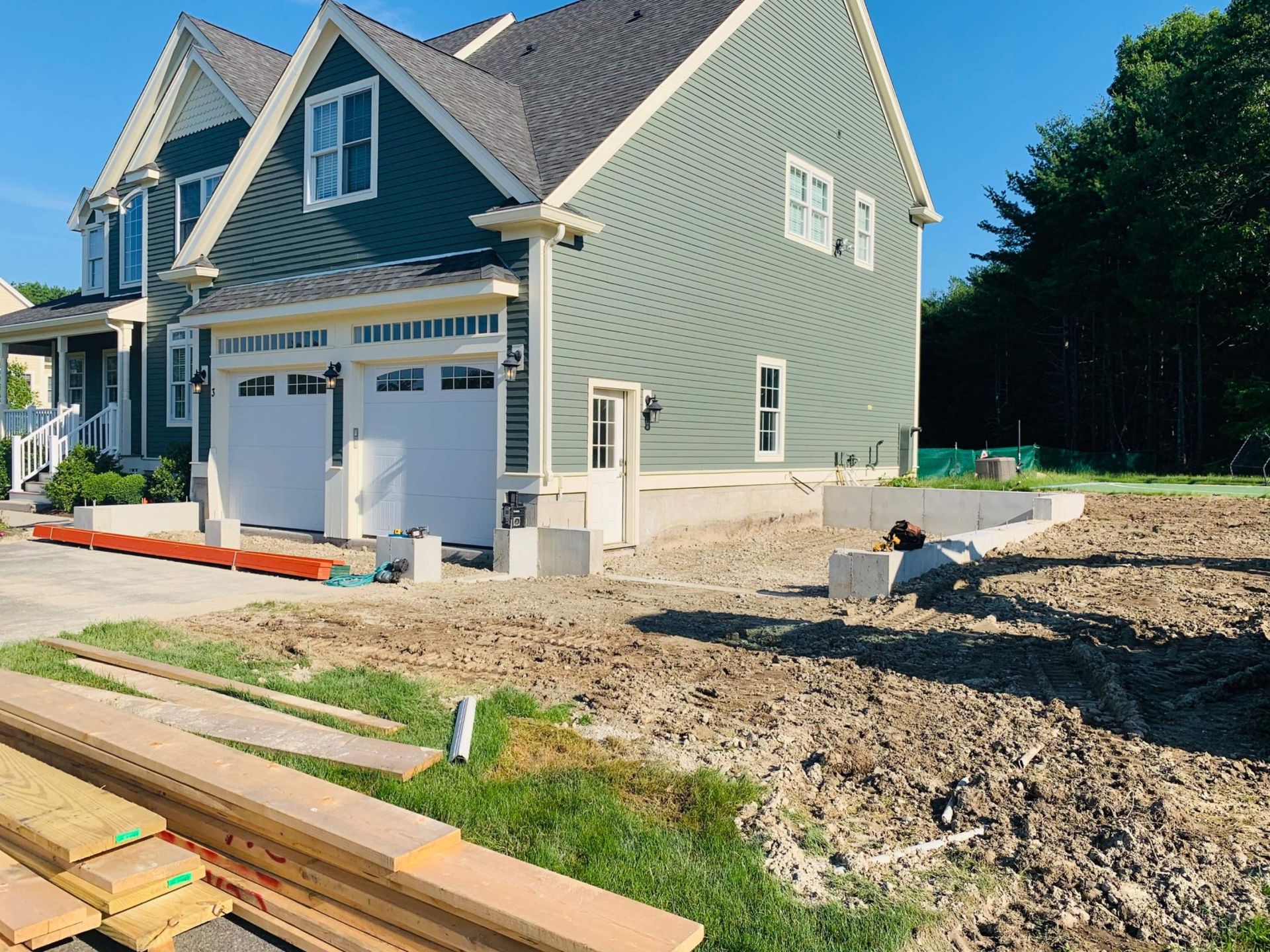 Newly constructed two-car garage with white doors, teal siding, and a partially finished driveway.