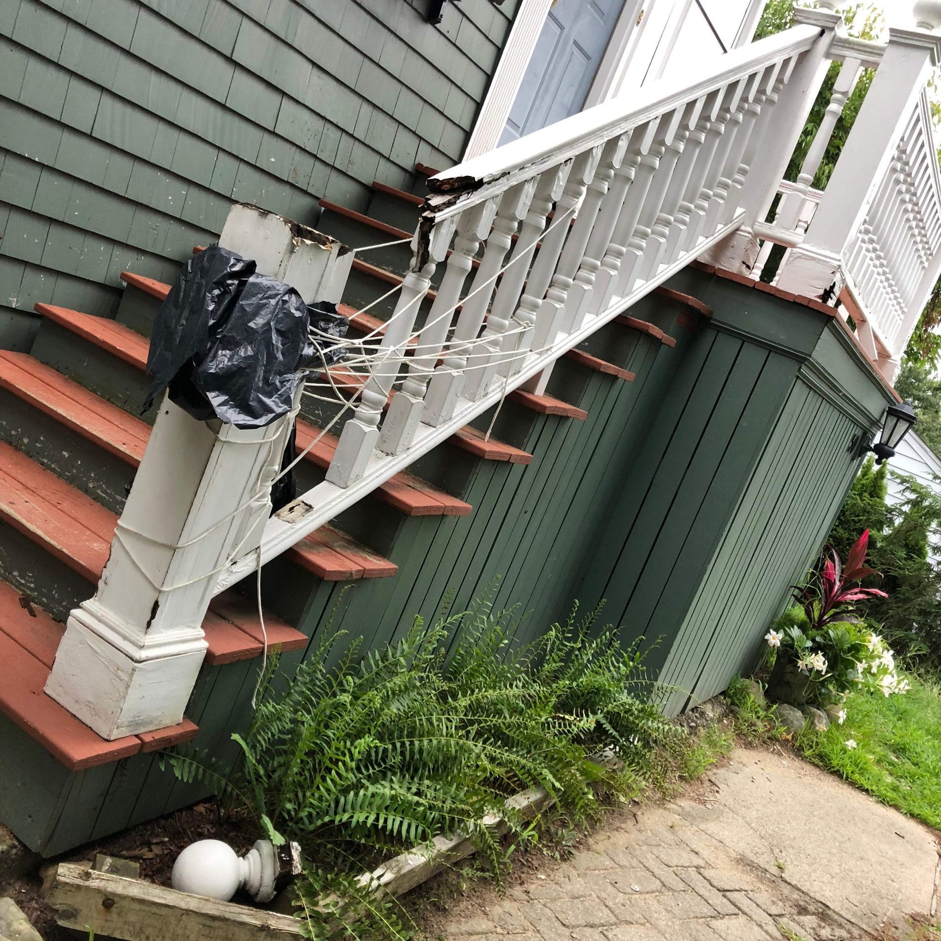 Exterior staircase with white railing, red steps, green siding, and a black trash bag.