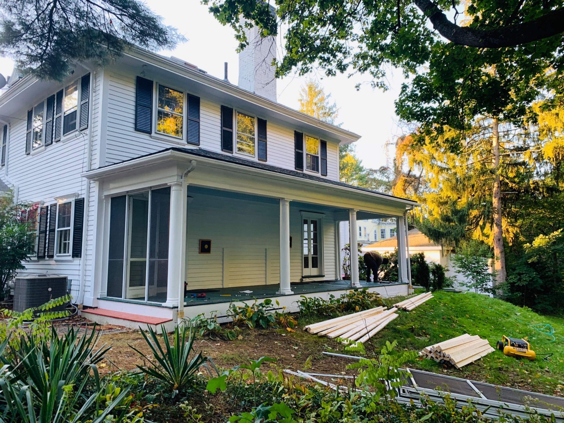 White house with screened porch, dark shutters, construction materials on lawn.