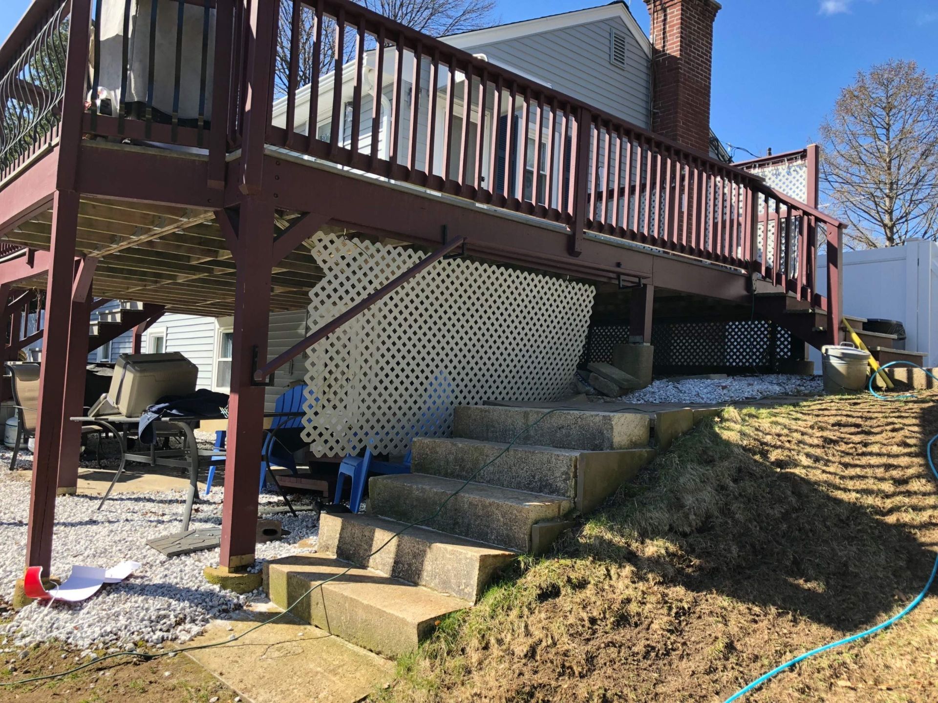 Deck with stairs descending a hillside. Lattice work and railing visible; house in background.
