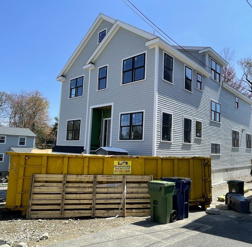 New three-story house under construction with a yellow dumpster and pallets in front.