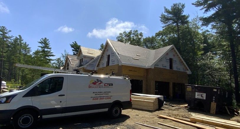 Construction of a new house with a white van and materials. Green trees and blue sky background.