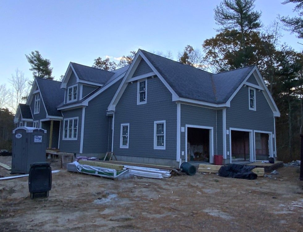 New house under construction, blue siding, gray roof, two-car garage, porta-potty in yard.