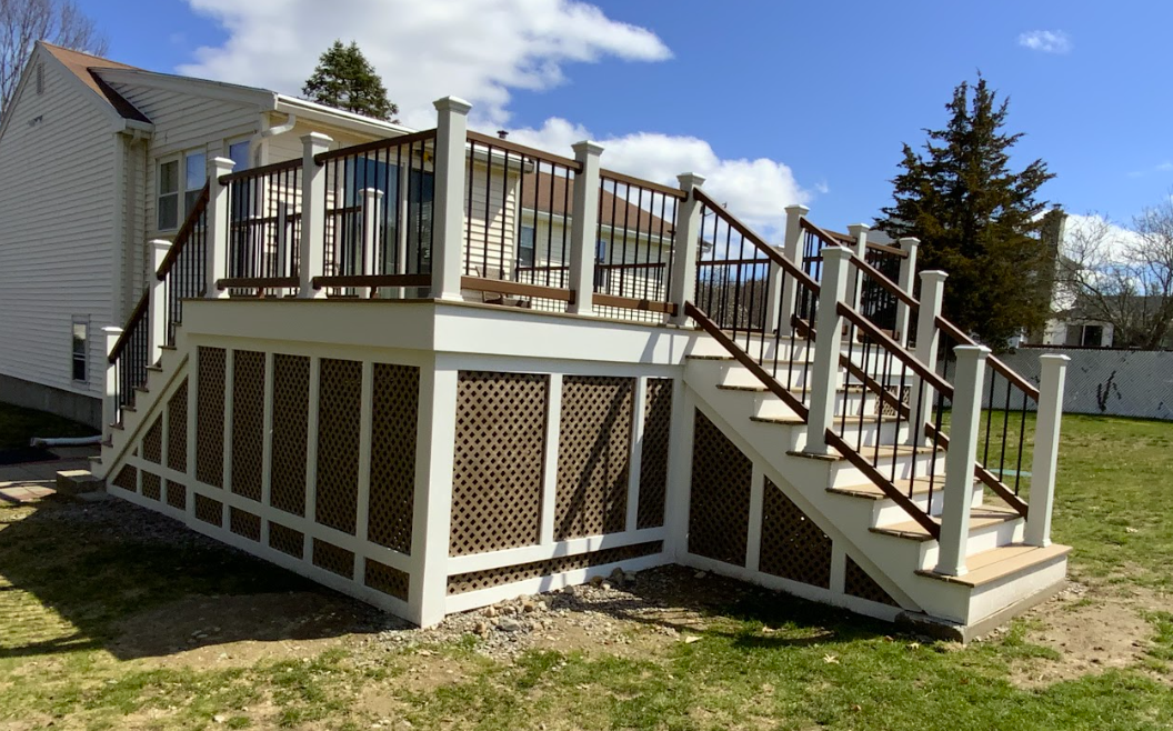 Two-level wooden deck with stairs and lattice skirting, against a white house. Sunny day.