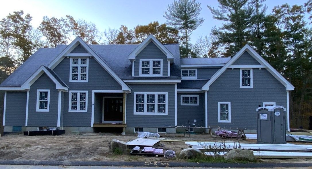 New construction house with gray siding, white trim, and a blue roof.