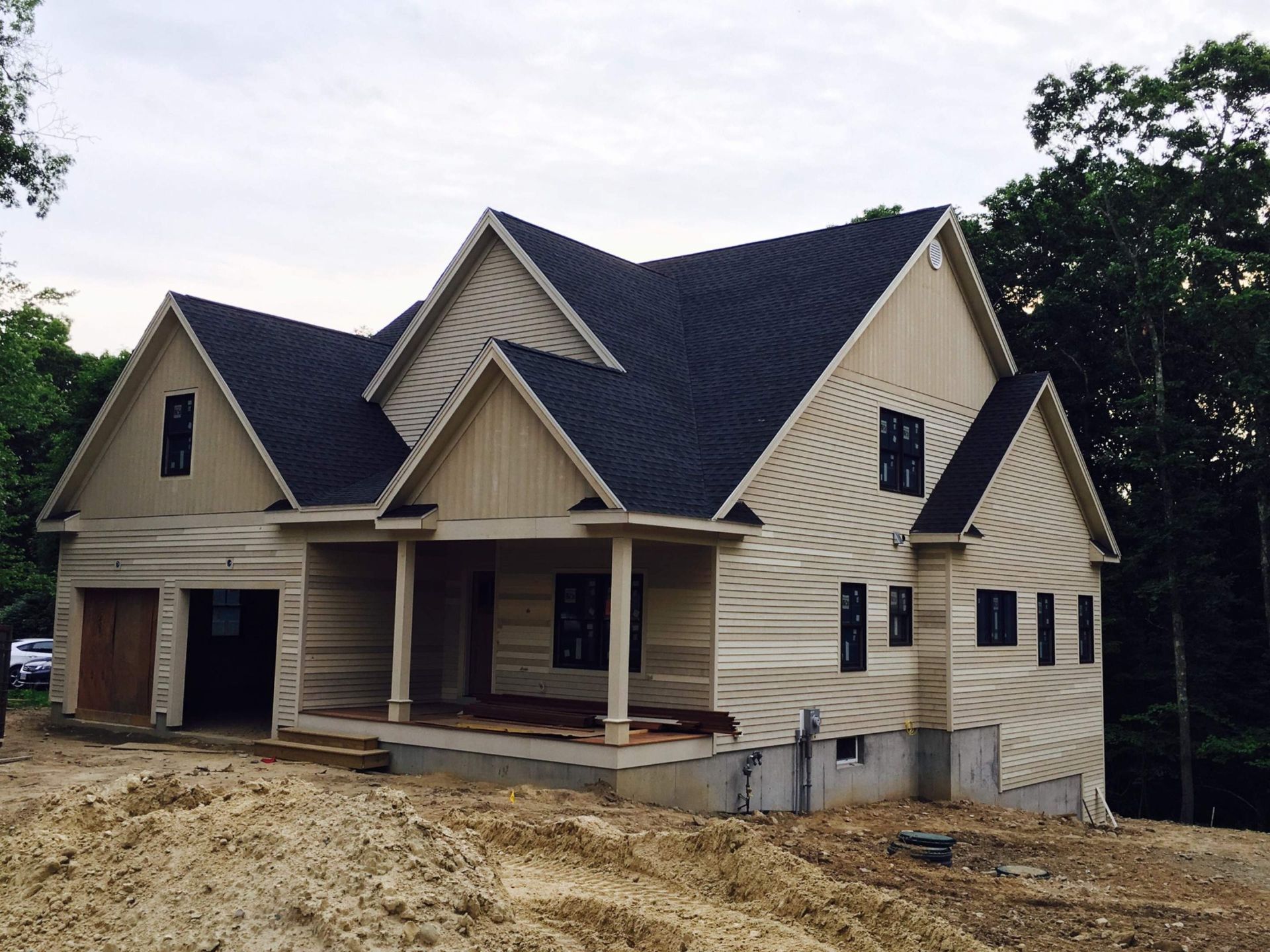 Newly constructed house with tan siding, dark roof, and covered porch, set on a graded lot.