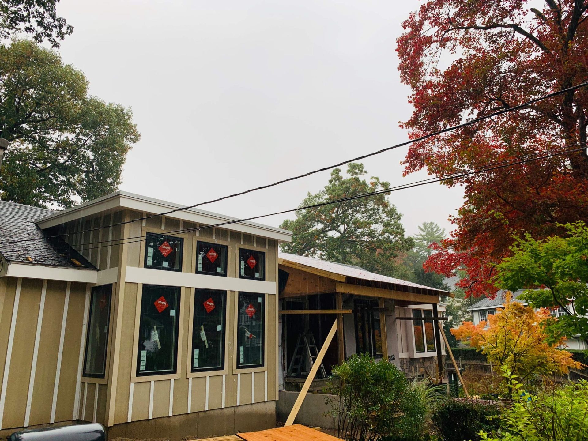 House under construction with exposed framing, windows, and autumn foliage.