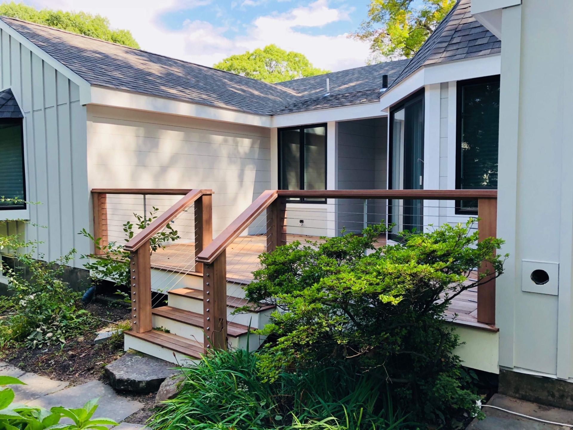 Exterior view of a house with a wooden deck and steps, surrounded by greenery.