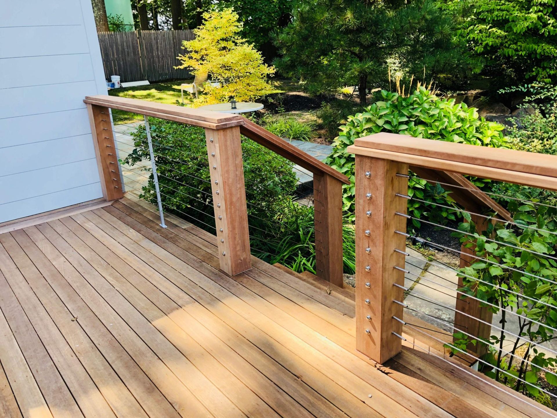 Wooden deck with cable railings and steps, surrounded by greenery.