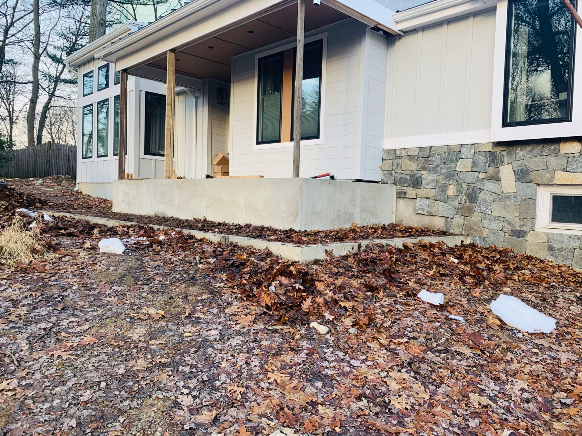 House exterior with concrete porch, stone base, and leaves on the ground.