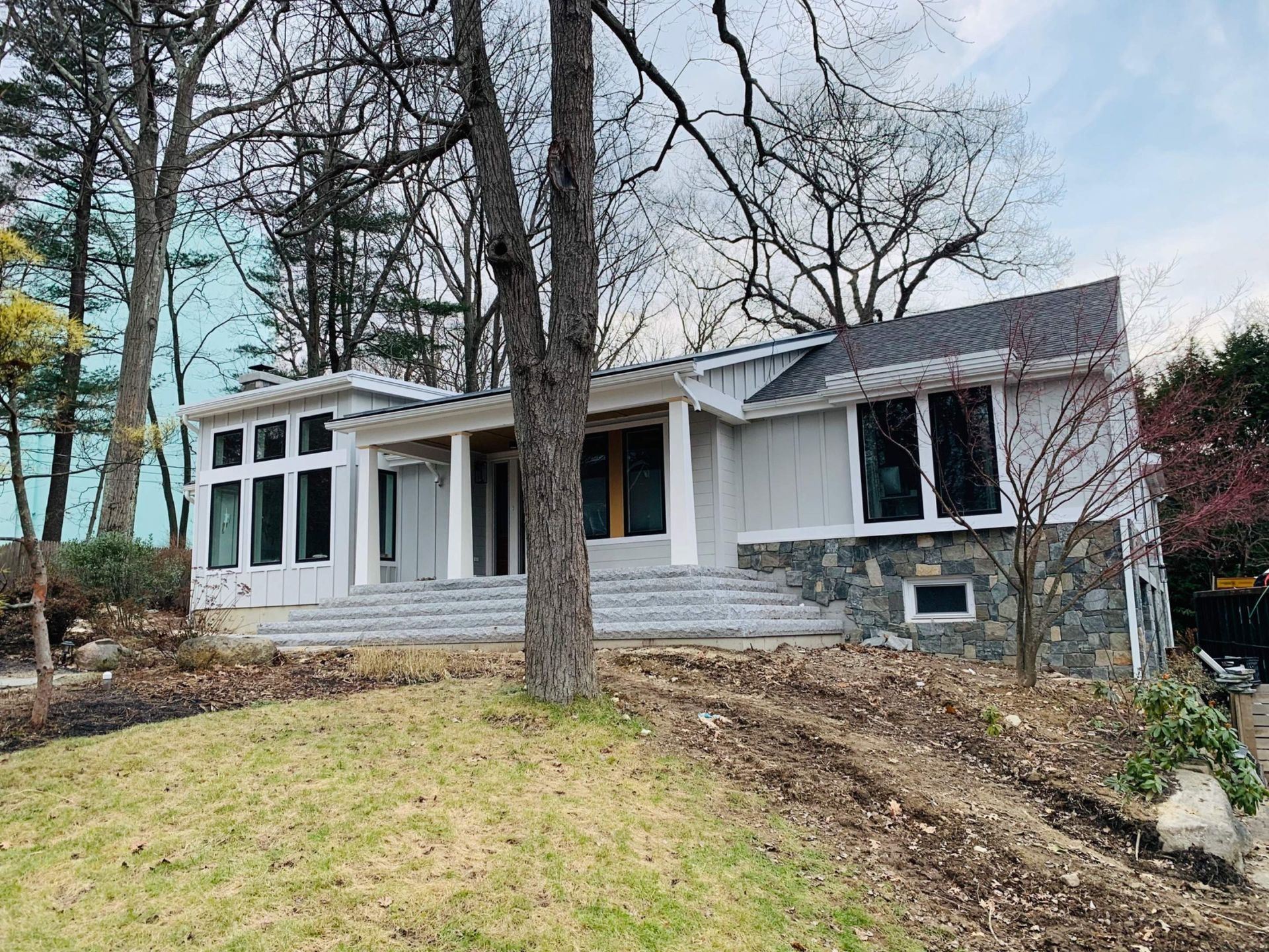 A light gray house with stone accents, a porch, and a grassy yard. Trees surround the building.