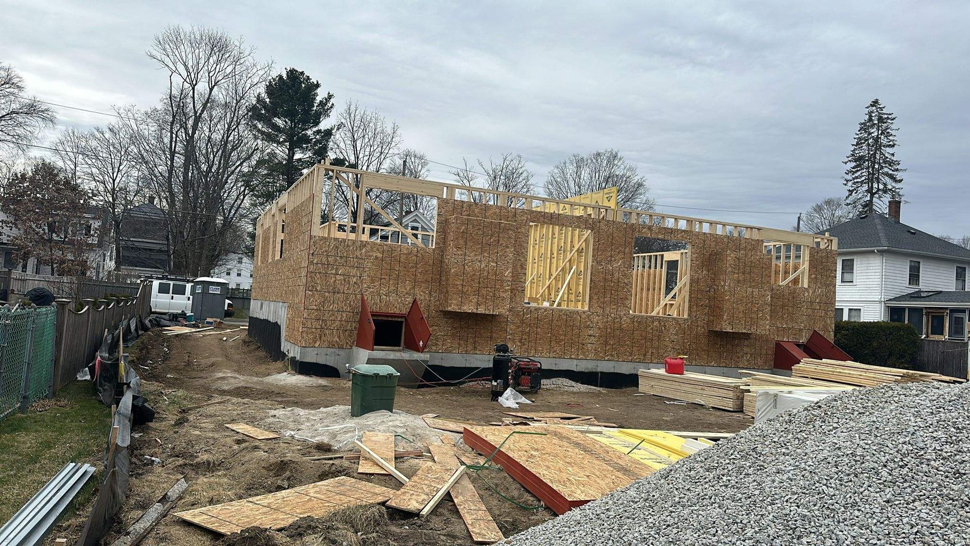 Construction site with wooden frame of a house, surrounded by building materials, under cloudy skies.