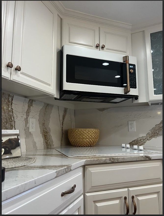 White kitchen cabinets with a white microwave above a countertop.