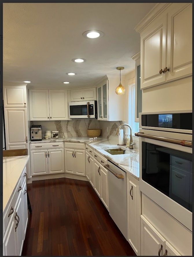 White kitchen with marble countertops, dark wood floors, and built-in appliances.