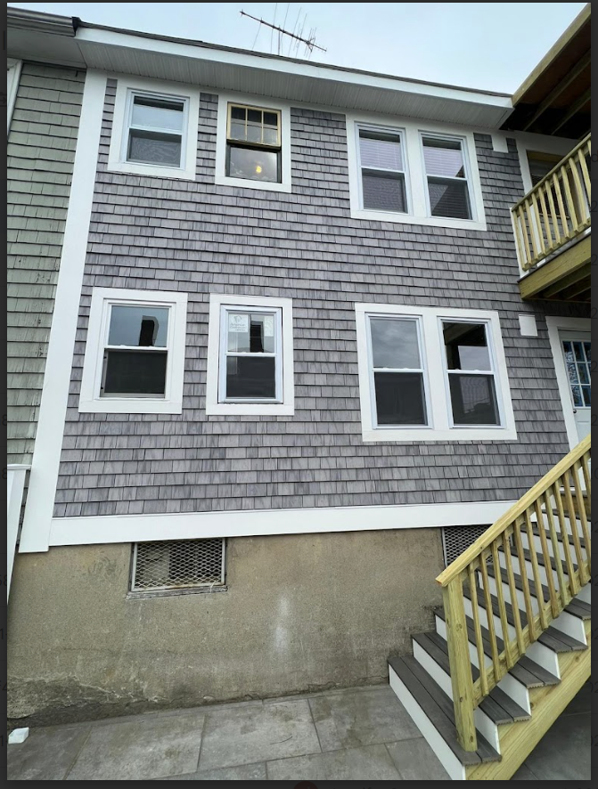 Gray shingled building exterior with white-trimmed windows and wooden stairs leading up.